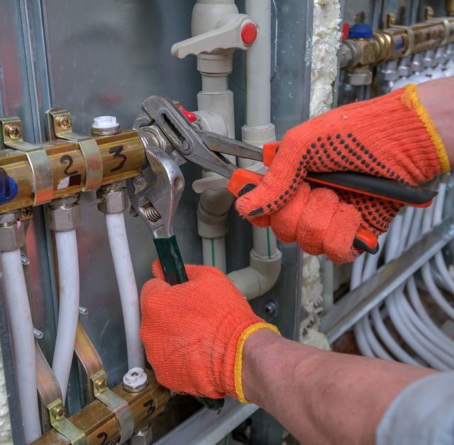 Zwei Hände in roten Handschuhen arbeiten mit Zangen an Rohren